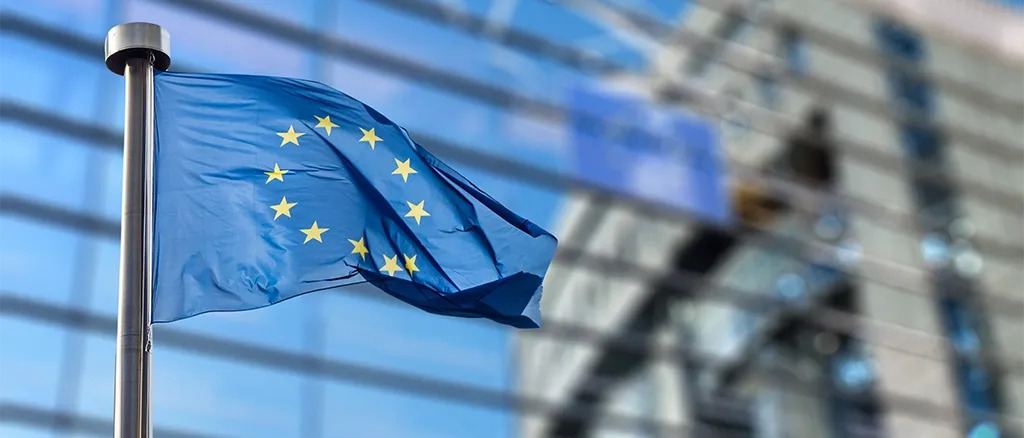 Flaga Unii Europejskiej powiewająca przed budynkiem z przeszkloną fasadą