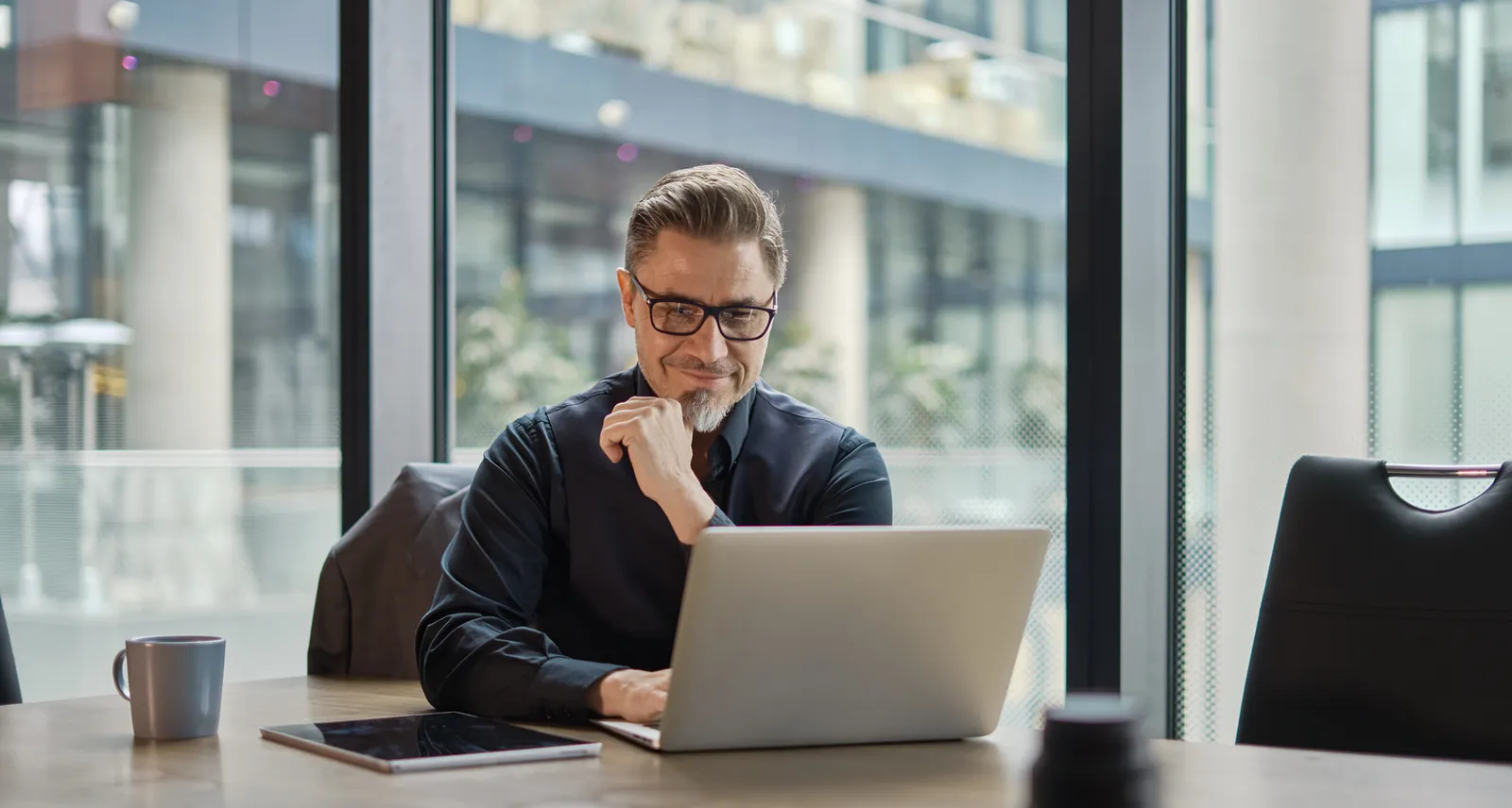 Ein Mann sitzt in einem hellen Büro am Laptop und lächelt beim Lesen