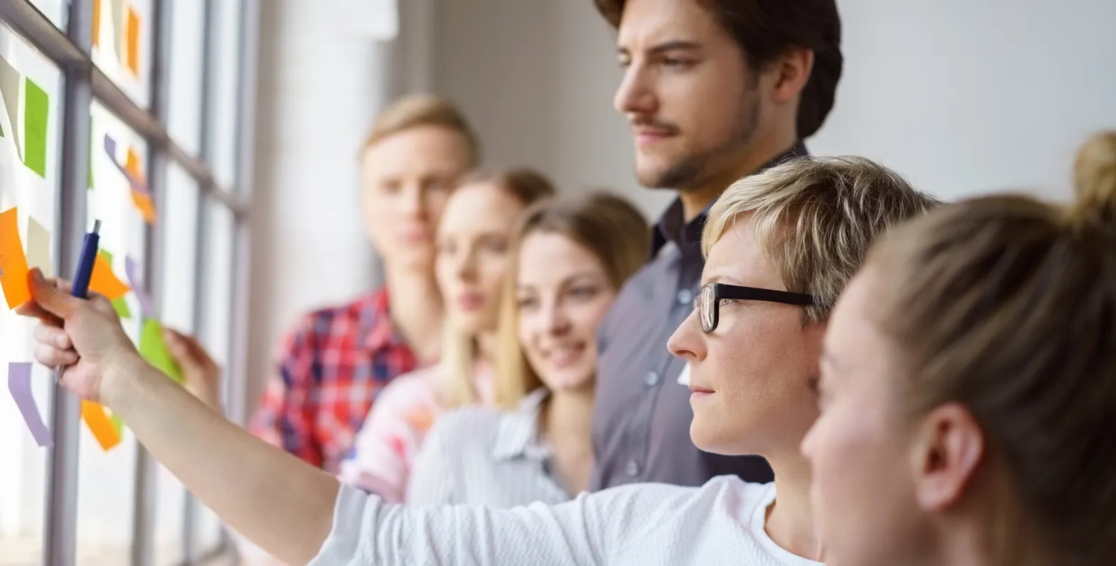 Ein Team steht an einer Glaswand mit bunten Haftnotizen und plant gemeinsam