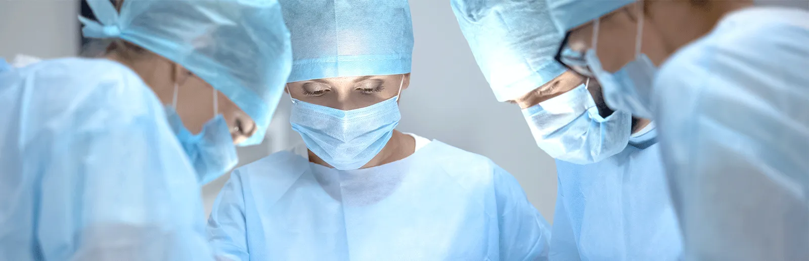 Zespół chirurgiczny w niebieskich czepkach, maskach i fartuchach skupiony nad stołem operacyjnym